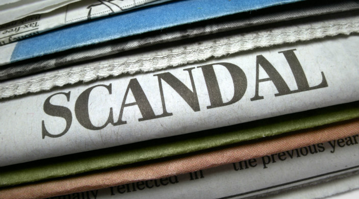 Stack of newspapers with one prominently proclaiming a scandal